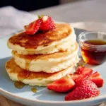 Fluffy pancakes stacked on a plate, drizzled with syrup and topped with fresh berries.