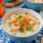 Bowl of Thai breakfast rice soup with shrimp, garnished with herbs